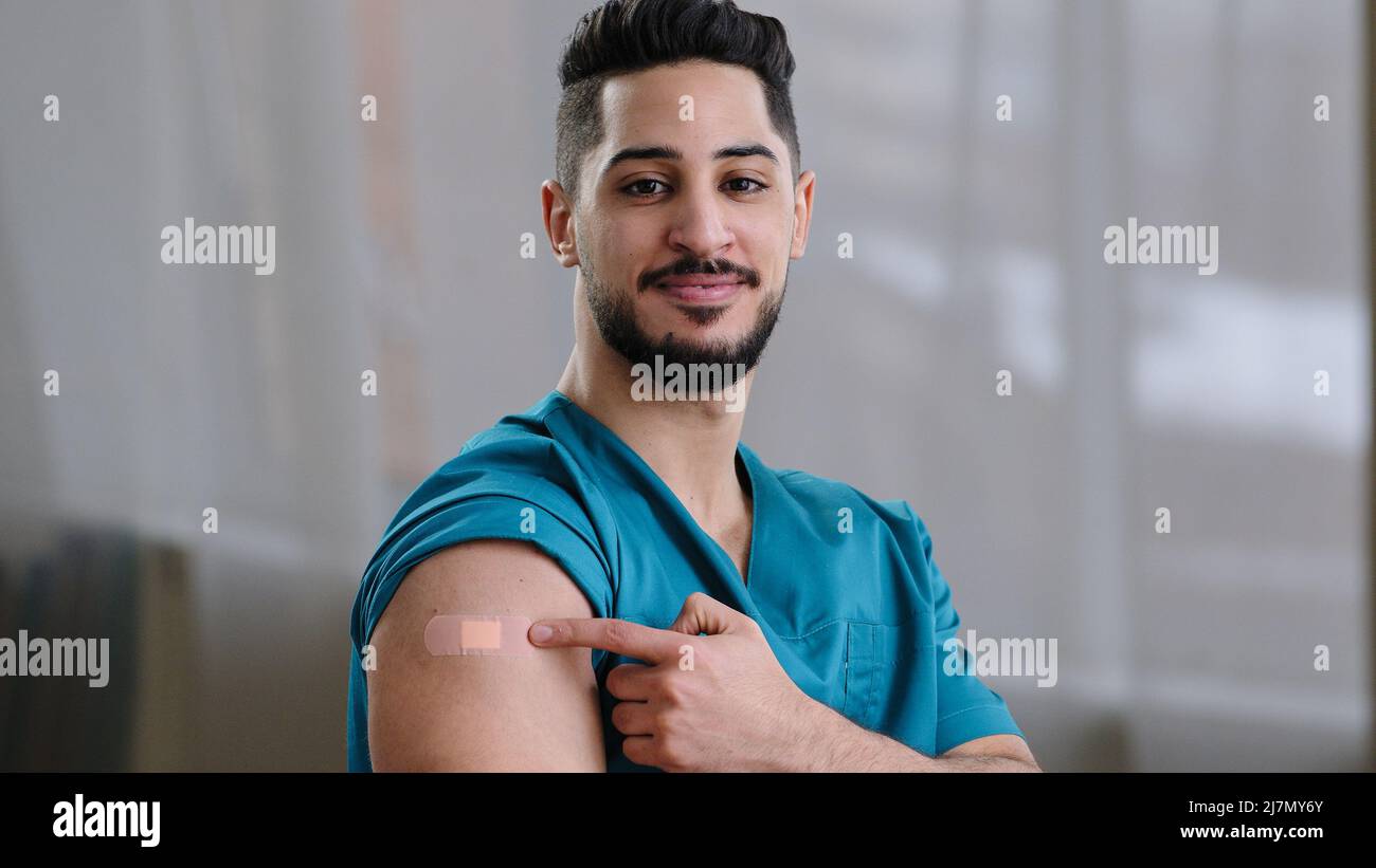 Ispirato lavoratore medico maschio arabo vaccinato da uomo virus covid-19 guardando la macchina fotografica che dimostra patch su spalla iniezione marchio vaccino Foto Stock