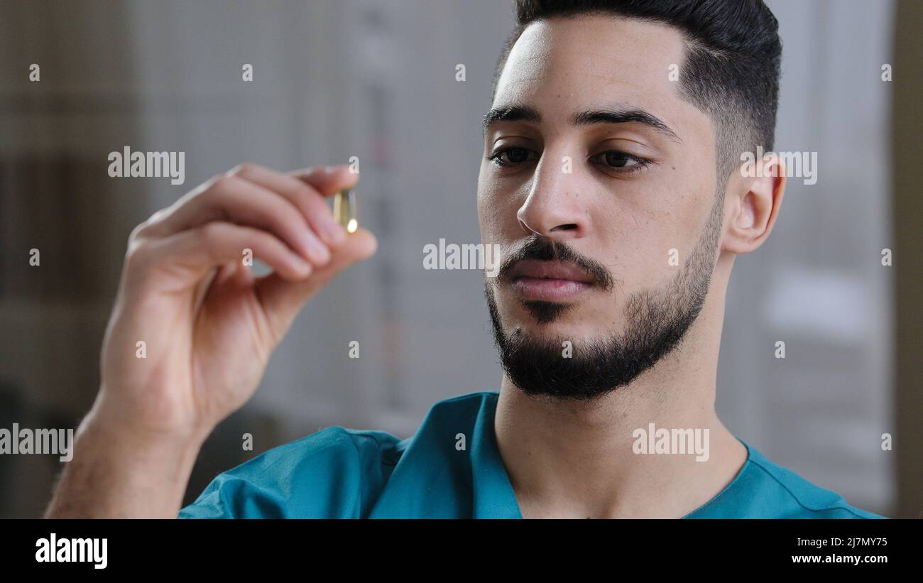 Giovane scienziato uomo ispanico medico dipendente tenendo in mano limpida capsula trasparente compressa in mano medico arabo analisi studiare le proprietà della droga Foto Stock
