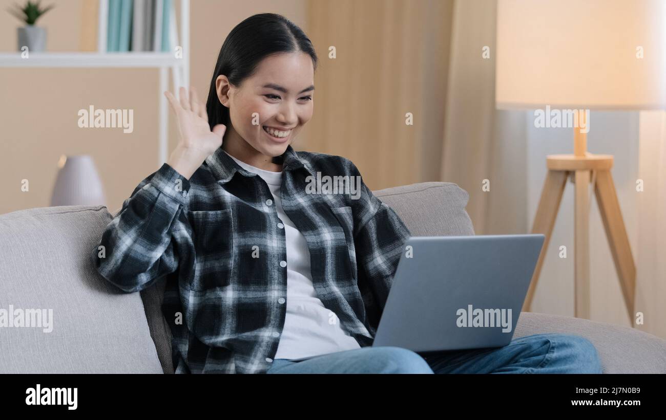 Asian sorridente donna d'affari freelance studente online insegnante psicologa ragazza donna seduta sul divano a casa teleconferenza videochiamata conversazione app Foto Stock