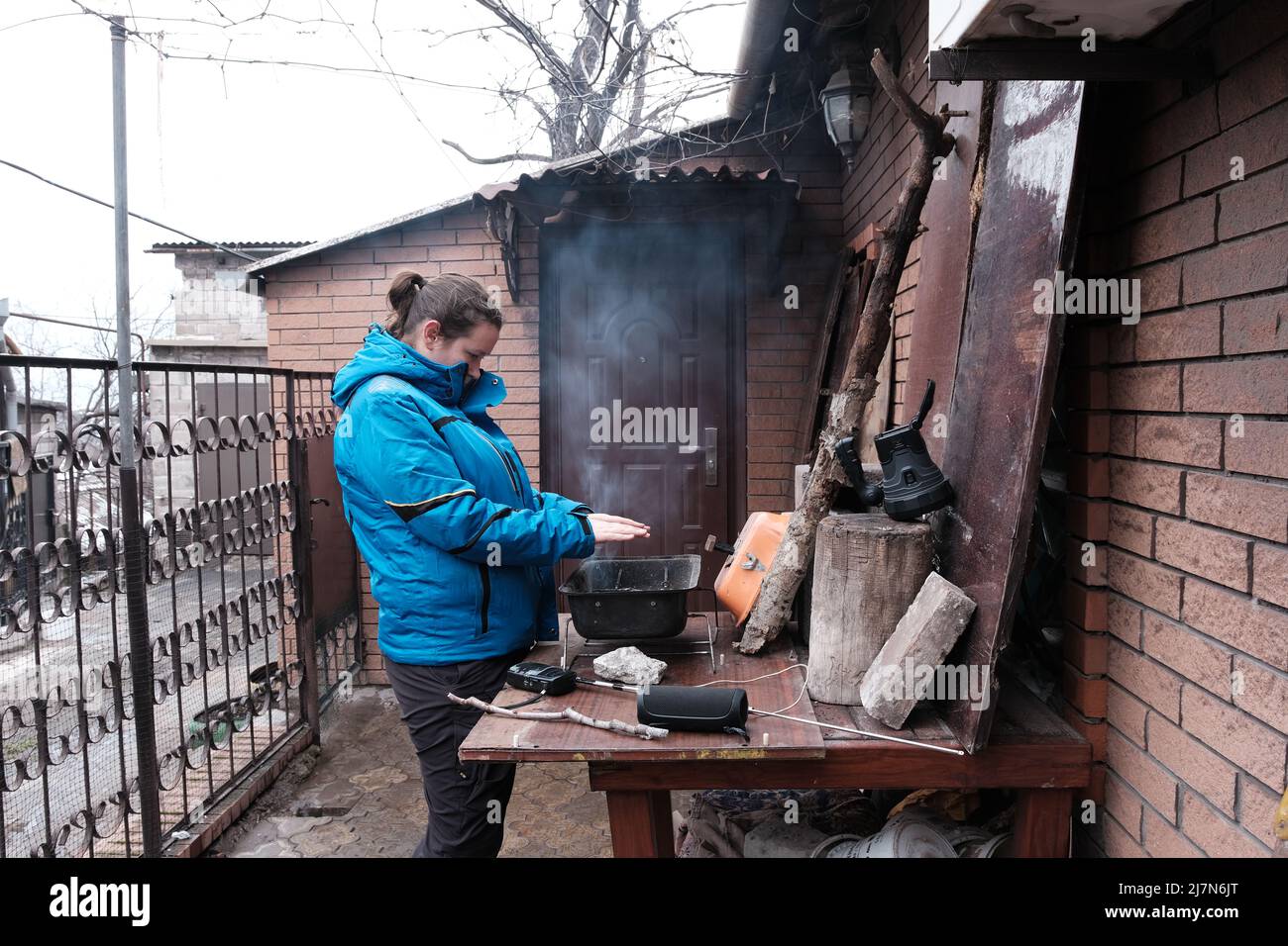 Mariupol, Ucraina - 5 marzo 2022: La donna si riscalda intorno a un falò sotto bombardamento della città di Mariupol, Ucraina. Foto Stock