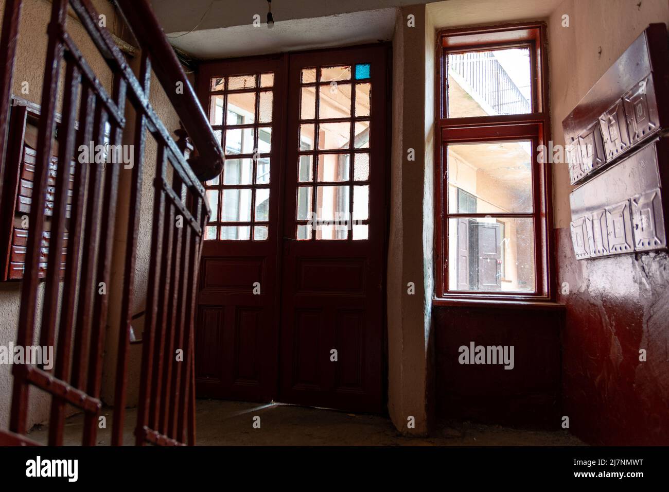 Foto all'interno del corridoio di un vecchio edificio di appartamenti, il sole splende attraverso le finestre e la porta d'ingresso, vecchio dipinto marrone e pavimento in pietra. Foto Stock