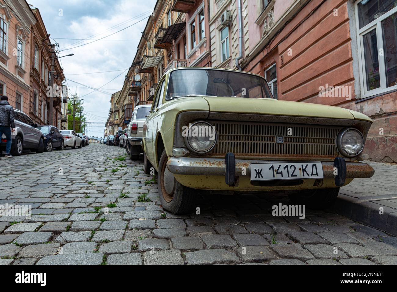 Ucraina, Chernivtsi, 03.27.2022: Strada con auto parcheggiate nella città di Chernivtsi. Vecchia auto Moskvich in primo piano. Strada acciottolata della città e ancien Foto Stock