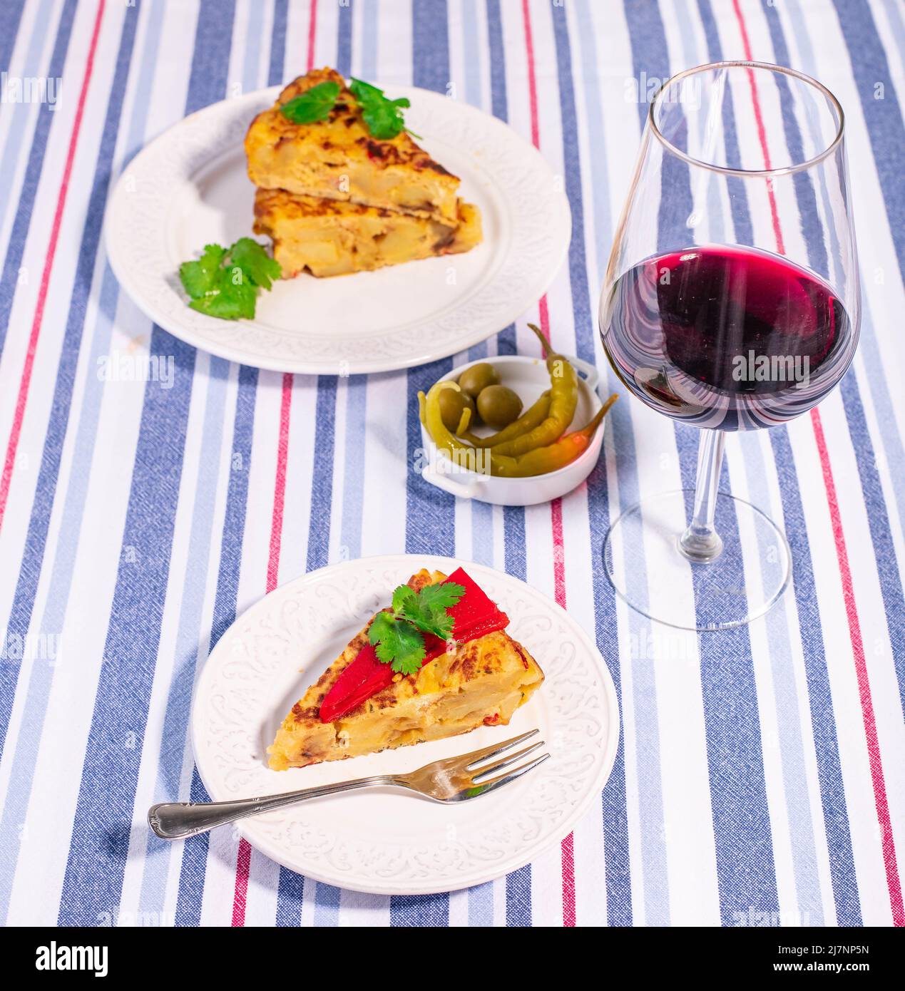 Tortilla patata tradizionale spagnola con peperoncino piquillo rosso, olive e guindilla piccante e un bicchiere di vino rosso. Foto Stock