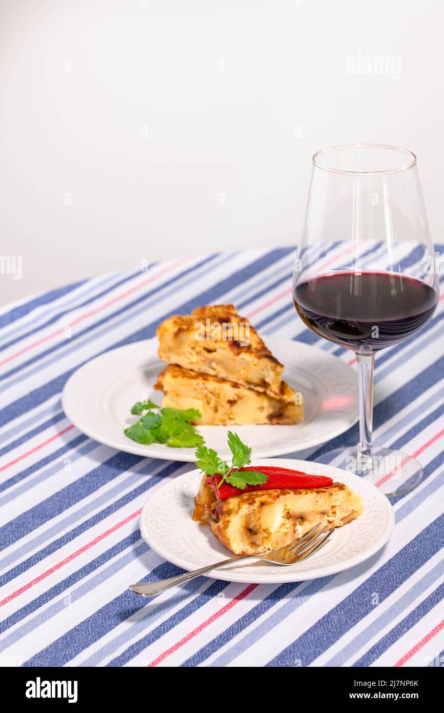 Tortilla patata tradizionale spagnola con peperoncino piquillo rosso, olive e guindilla piccante e un bicchiere di vino rosso. Foto Stock