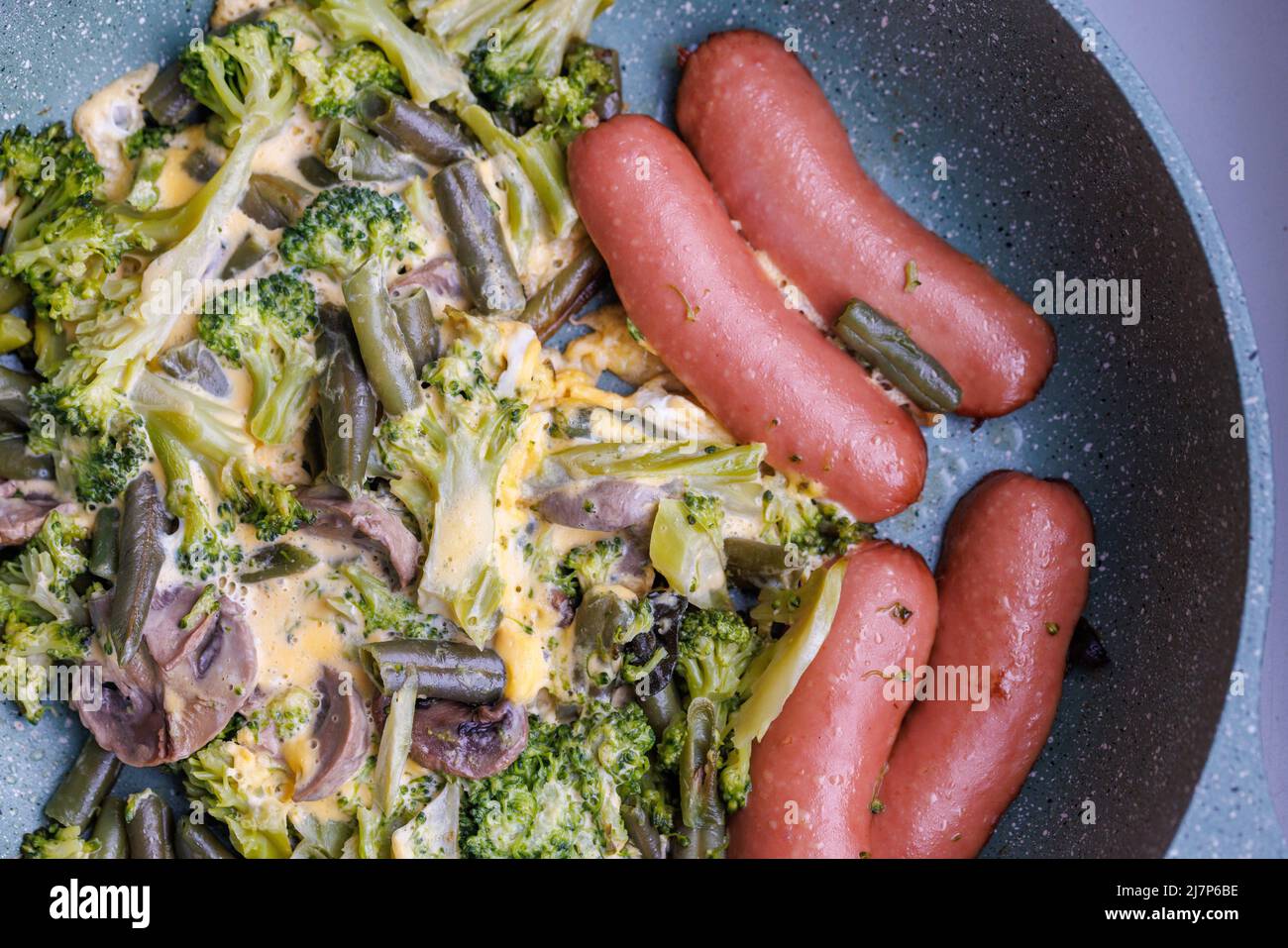 salsicce e verdure fritte con funghi e uova di pollo sulla padella Foto Stock