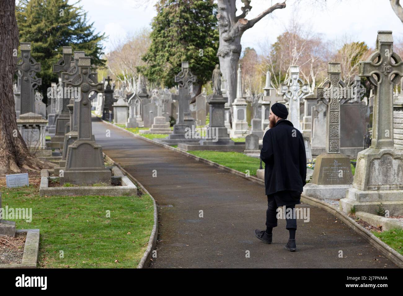 L'uomo in nero cammina davanti alle lapidi e ai luoghi di sepoltura al cimitero di Glasnevin Foto Stock