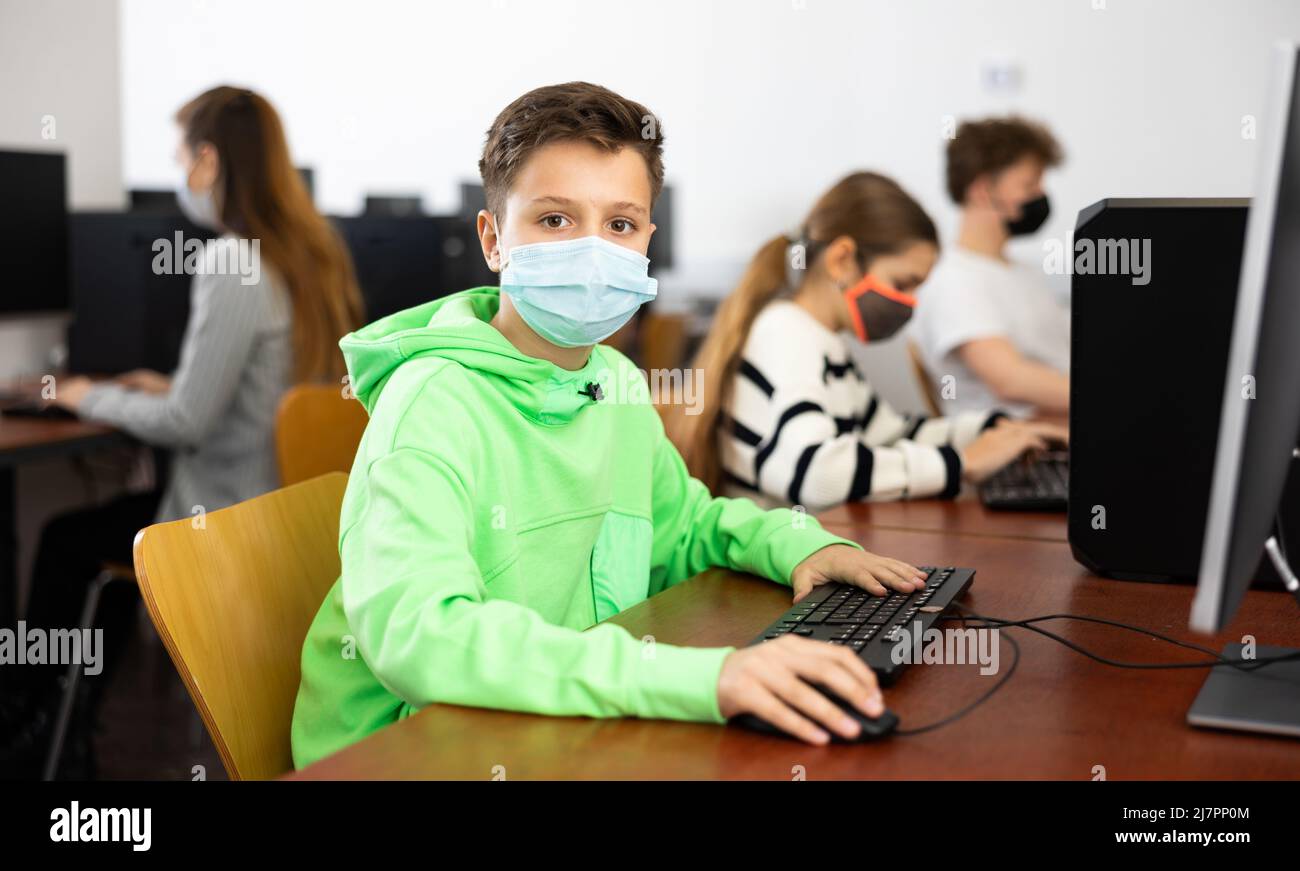 Tween ragazzo in maschera protettiva studiando in laboratorio computer Foto Stock