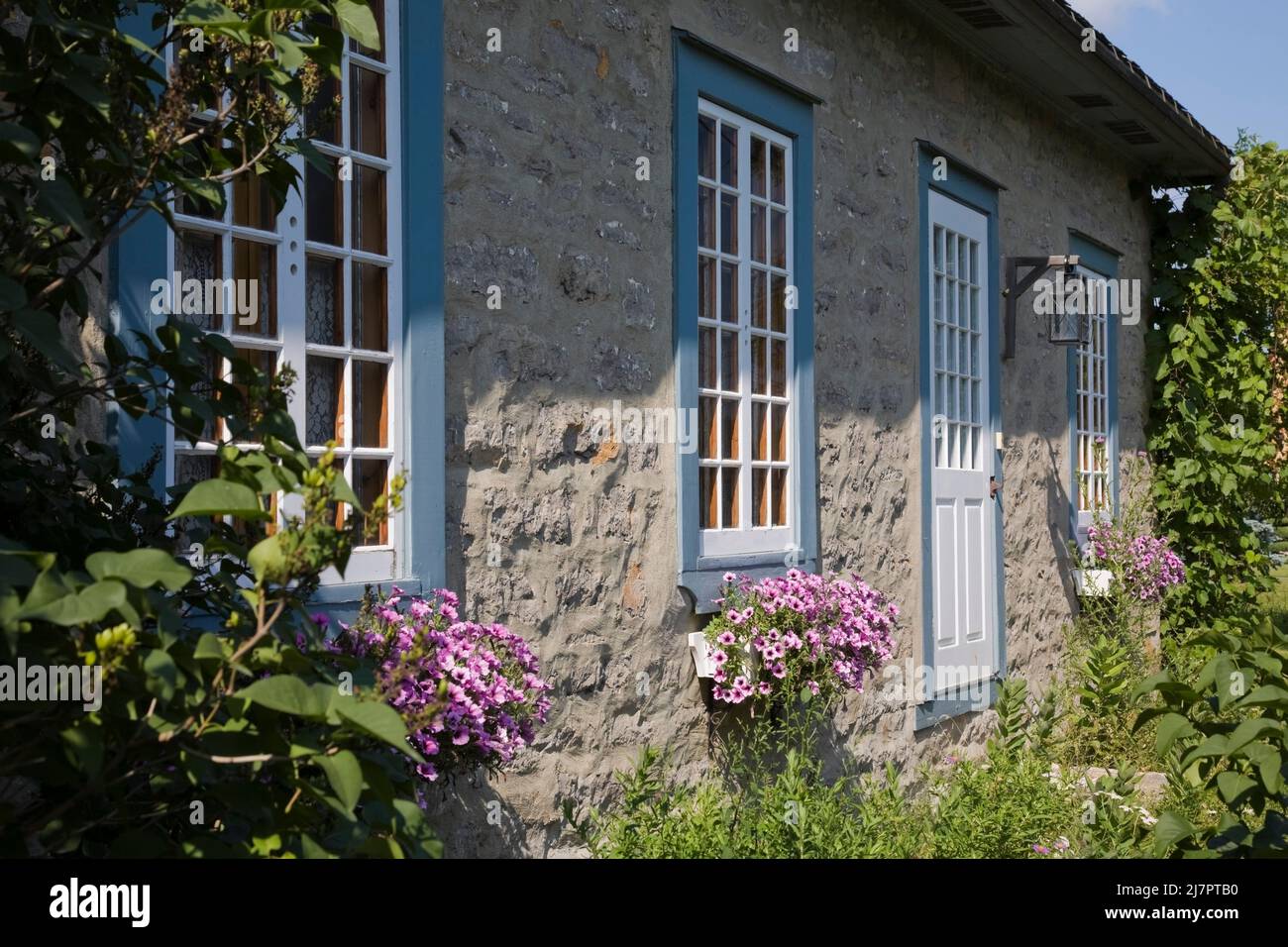 Vecchio circa 1850 Canadiana cottage stile fieldstone casa con finiture blu e bianco in estate. Foto Stock