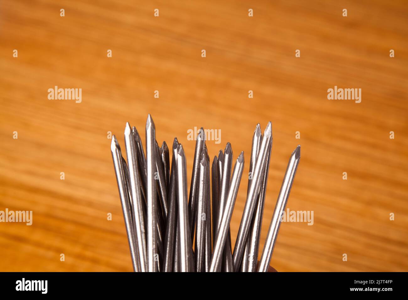 Ferro di metallo chiodo molto appuntito su legno di noce in, isolato su sfondo di legno Foto Stock