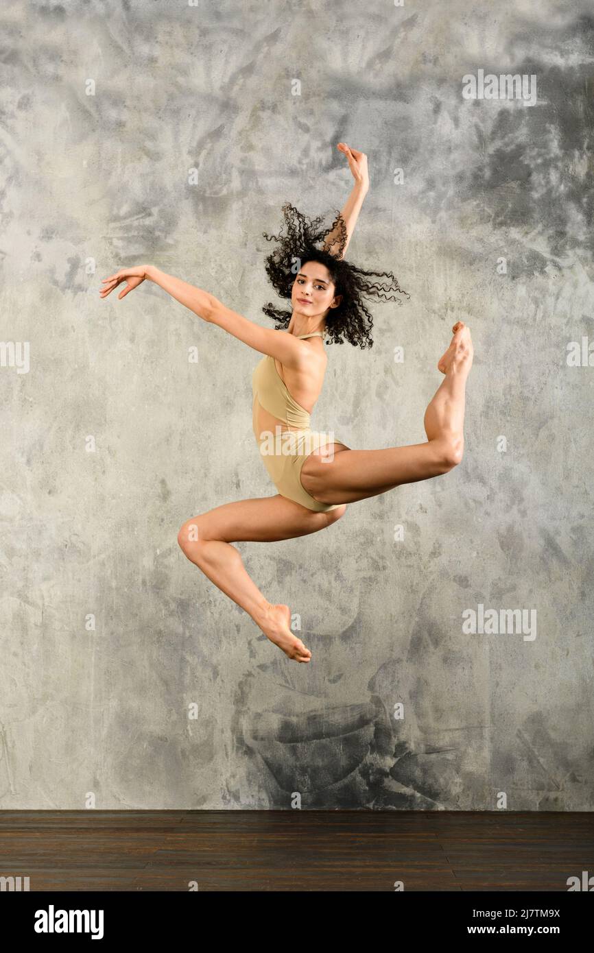 Ballerina agile a tutto corpo con le braccia che sollevano e saltano in alto mentre ballano contro la parete grigia grungy. Concetto di danza. Foto Stock