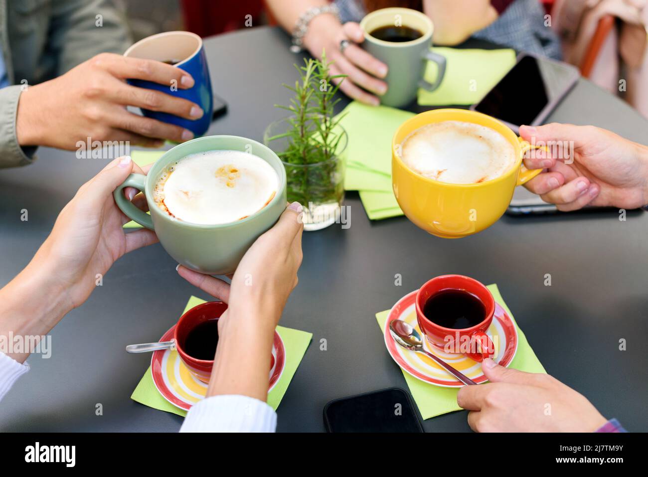 Ritagliate un gruppo irriconoscibile di amici che bevono caffè e cappuccino da tazze colorate mentre consumano la colazione insieme in una moderna caffetteria leggera Foto Stock