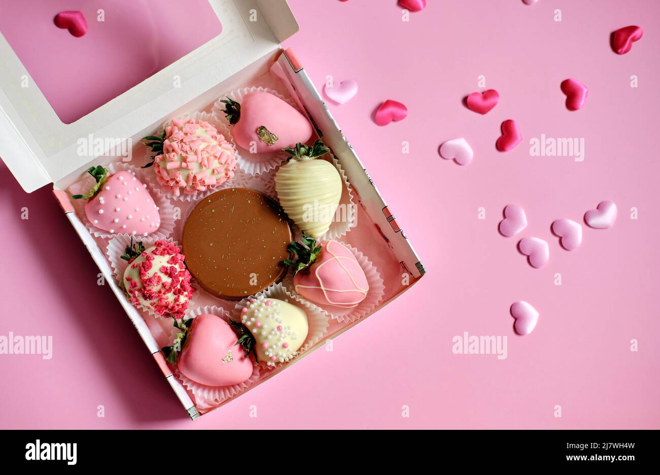 fragole in cioccolato in scatola con cuori sparsi su sfondo rosa. Dolce regalo per San Valentino Foto Stock