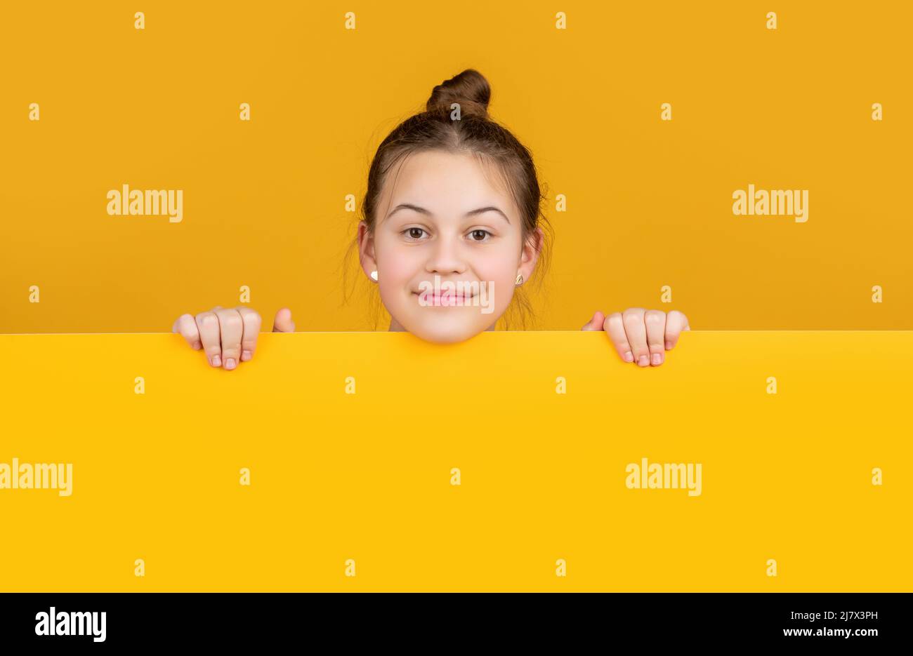 ragazza felice dietro carta bianca gialla con spazio per la copia per la pubblicità Foto Stock