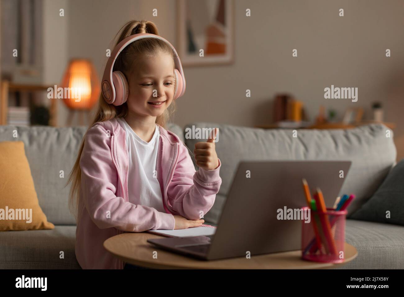 Little Schoolgirl usando il laptop gesturing Thumbs Up seduta a casa Foto Stock
