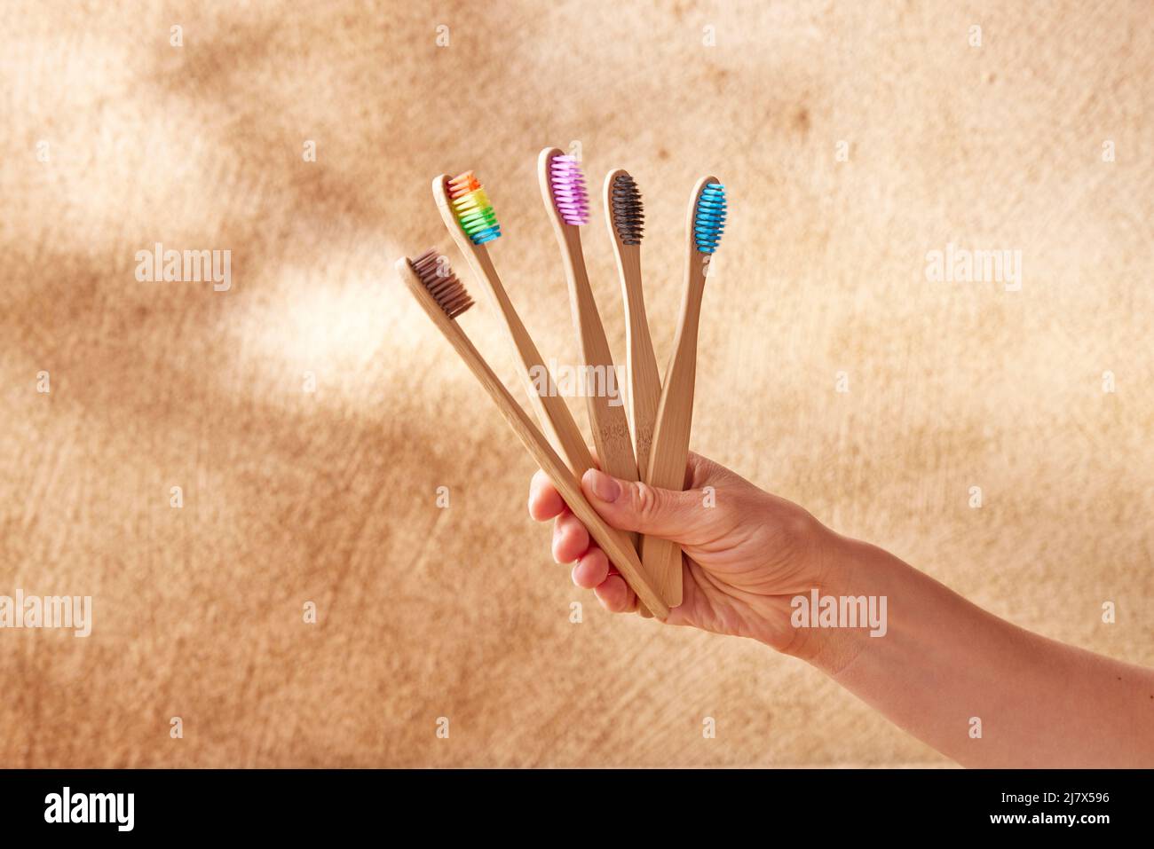 Donna anonima con set di spazzolini in bambù naturale multicolore assortiti per una cura orale quotidiana ecologica su sfondo beige Foto Stock
