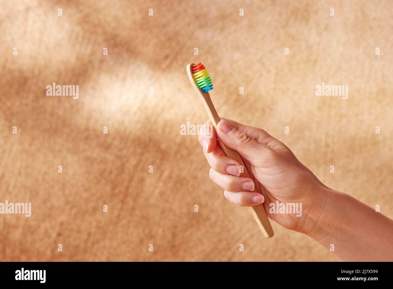 Ritagliare una donna irriconoscibile che mostra uno spazzolino di bambù ecologico con setole colorate su sfondo beige sfocato Foto Stock