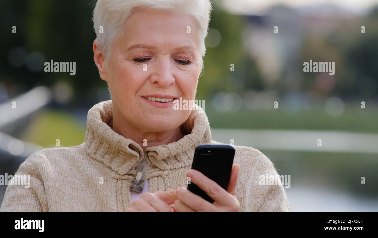 Closeup grigio-Haired Donna matura che texting messaggi su smartphone moderno gadget, scorrimento, touchscreen, sorpreso, nonna navigare in Internet su Foto Stock