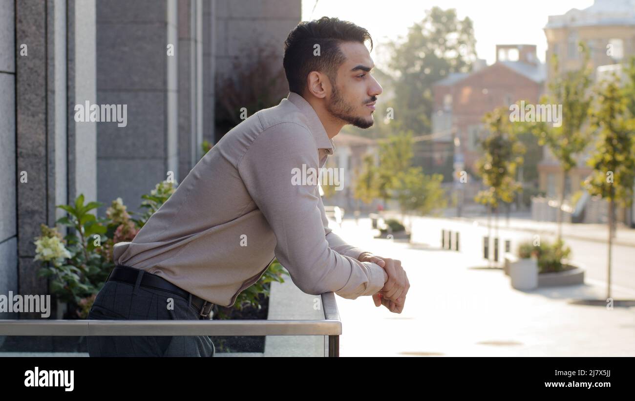 Felice pensivo riuscito rilassato uomo d'affari ispanico ragazzo maschio arabo investitore uomo d'affari si leva sul balcone della terrazza nell'edificio d'ufficio in camera d'albergo Foto Stock