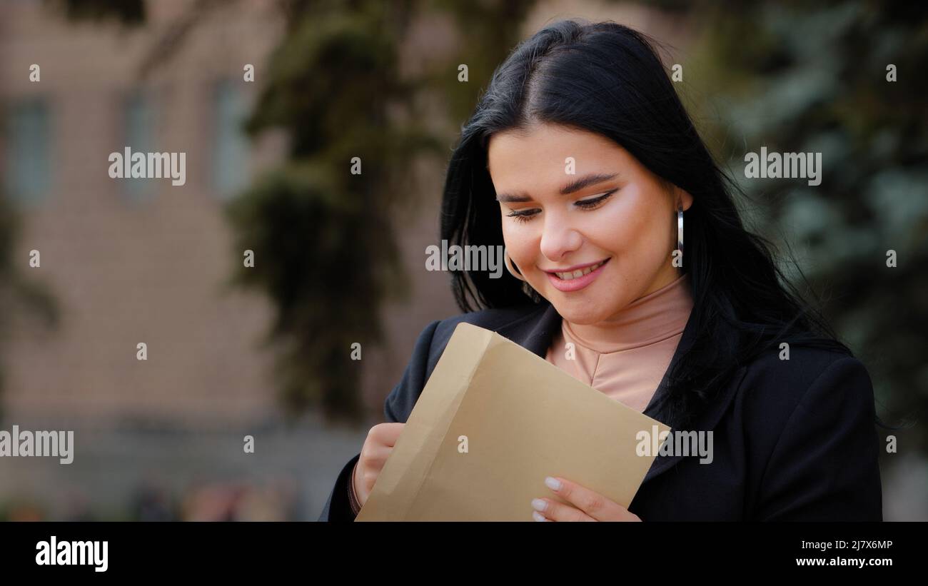 Ispanica giovane donna seduta su strada apre carta lettera leggere buone notizie bella ragazza felice sorridente femmina ha ottenuto sogno di carriera di crescita a Foto Stock