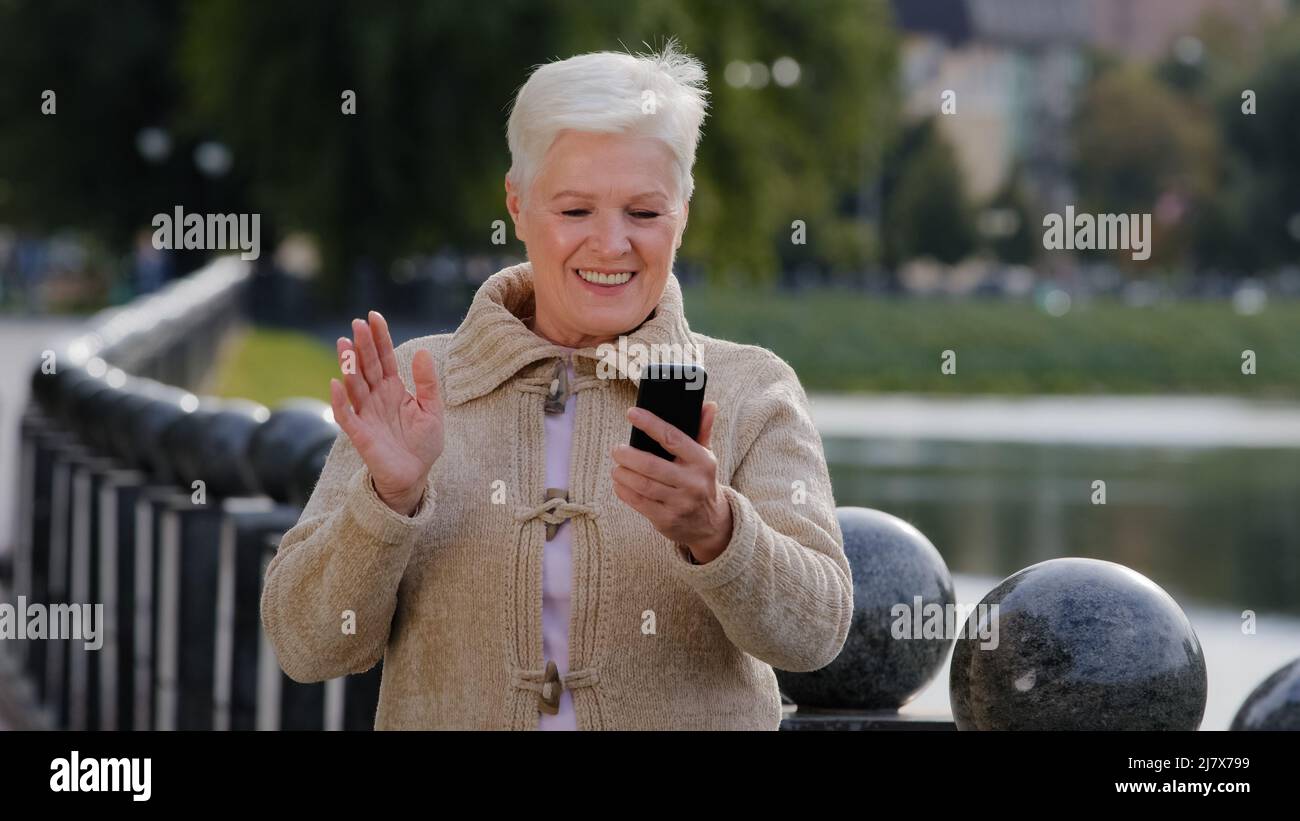 Donna anziana felice di età pensionabile che fa videochiamata, guardando la fotocamera dello smartphone. Attraente vecchia matura donna utilizza moderno gadget wireless Foto Stock