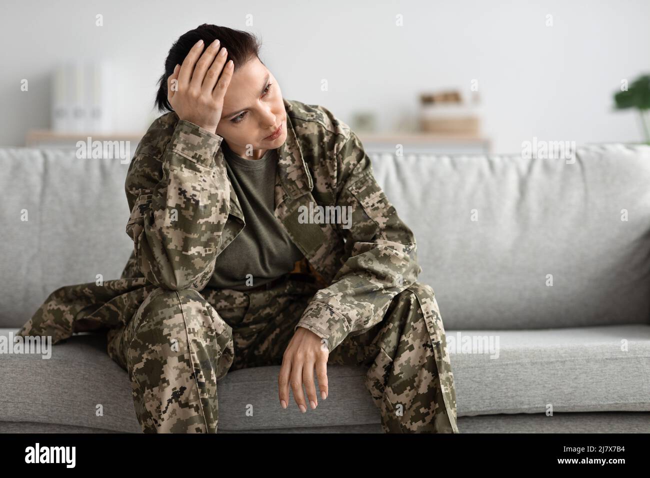 Impatto del Servizio militare. Soldier femminile depressa e pensiva seduta sul divano Foto Stock