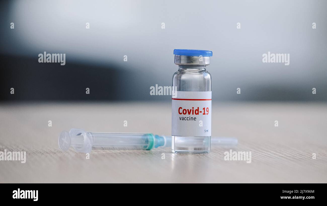 Primo piano flacone di vetro trasparente con vaccino del coronavirus covid-19 supporto su medicinale da tavolo e siringa preparazione per l'iniezione della vaccinazione Foto Stock