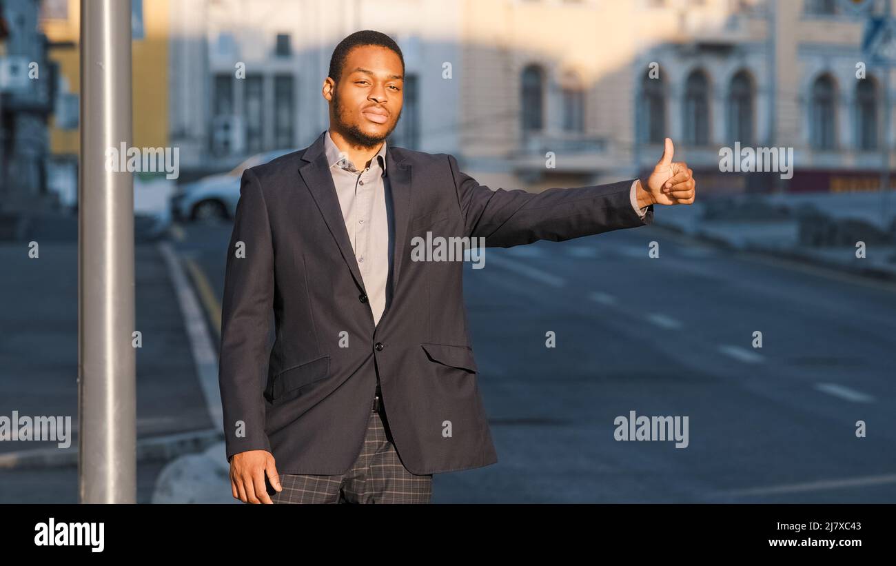 Attraente studente afroamericano, giovane ragazzo in abito in attesa di taxi all'aperto. Uomo d'affari moderno o direttore gesturing per dare il segnale al conducente dell'automobile Foto Stock