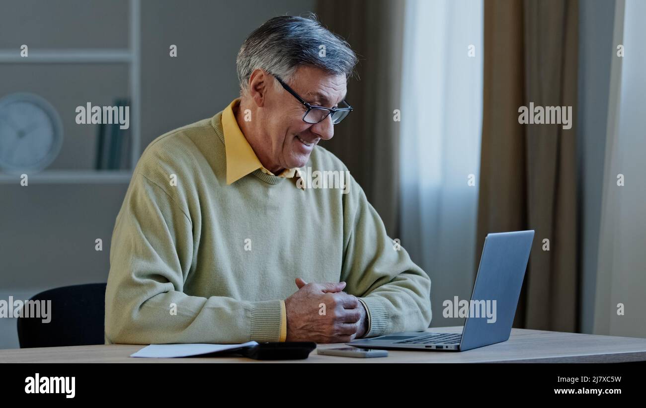 Primo piano-up uomo anziano negoziazione online utilizzare laptop professore insegnamento lezione su internet seduta a casa mostrando pollice in su soddisfa il lavoro in pensione maturo Foto Stock