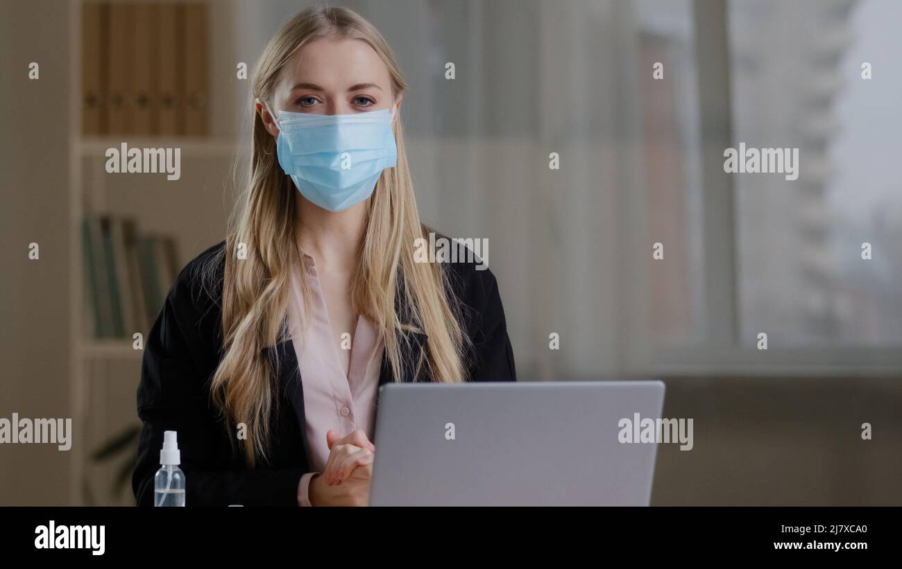 Divertente humorous lavoro donna in ufficio seduto al tavolo sente freddo che soffre di influenza virus mette su tre maschere protettive mediche paura Foto Stock