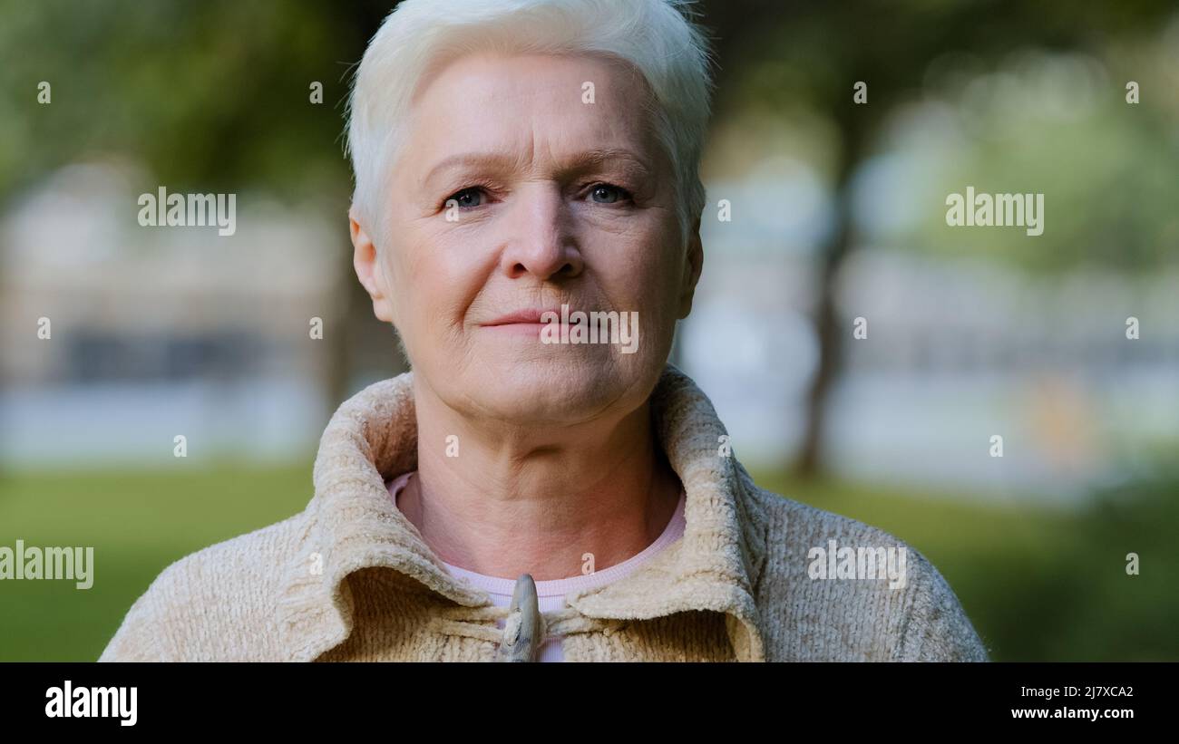 Primo piano ritratto di felice età bella donna guardando la macchina fotografica rilassante posa all'aperto in clima fresco, sorridente donna anziana donna sensazione di signora Foto Stock