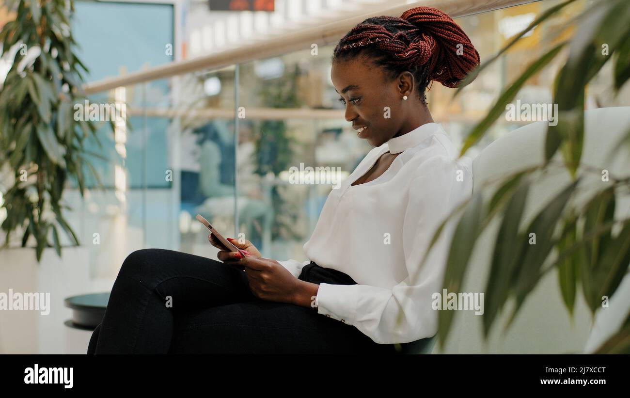 Felice donna d'affari african american ragazza lavoratore manager giovane donna seduta in corridoio ufficio moderno creativo azienda nel centro commerciale chatting Foto Stock
