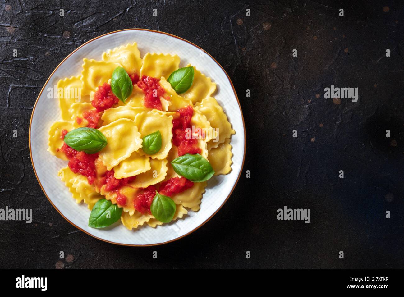 Ravioli con salsa di pomodoro e foglie di basilico fresco, colpo di testa con un posto per il testo. Ricetta italiana su sfondo ardesia nero Foto Stock
