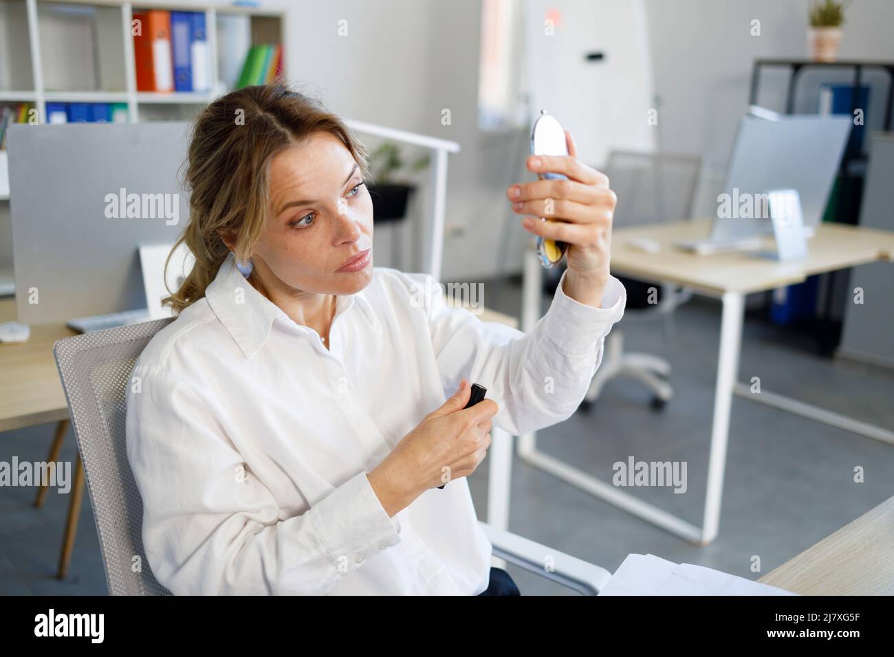 Bella donna matura con mascara in mano si guarda nello specchio Foto Stock