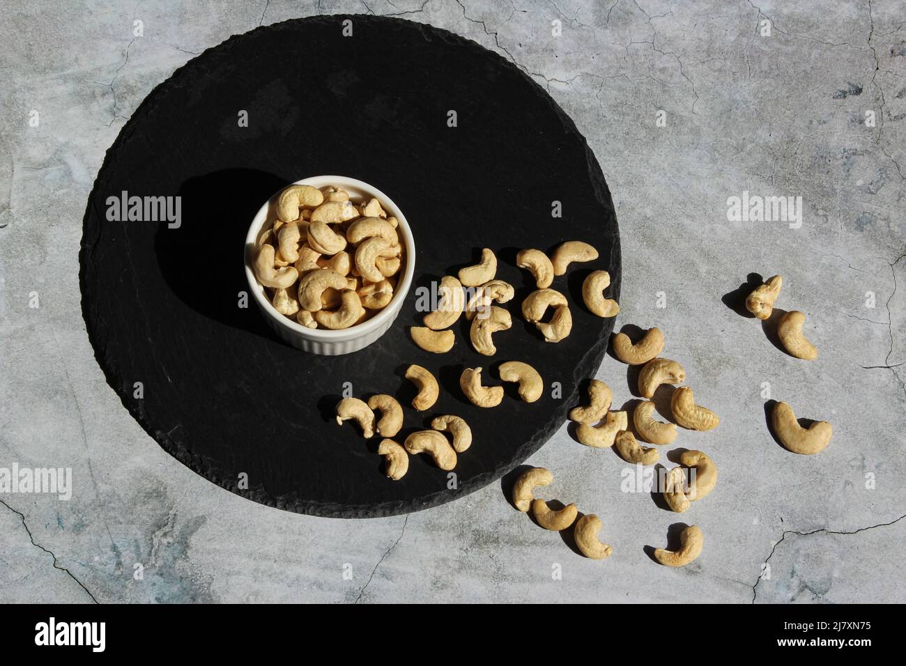 Dadi di cashew sulla piastra di pietra nera sullo sfondo di cemento. Vista dall'alto. Foto Stock