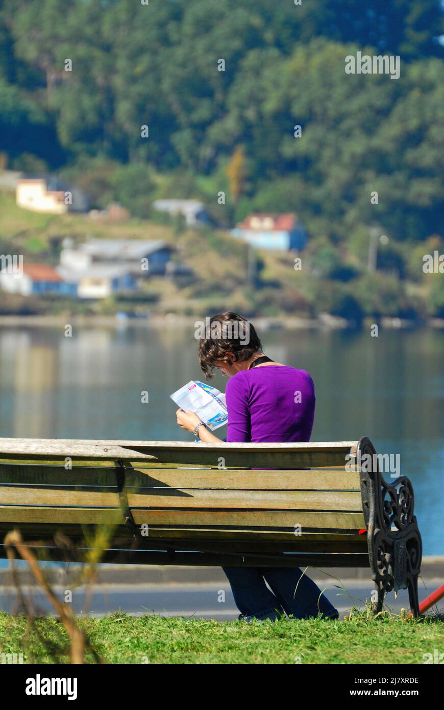 Vista posteriore di una donna seduta su una panca esterna leggendo una mappa turistica del Cile Foto Stock