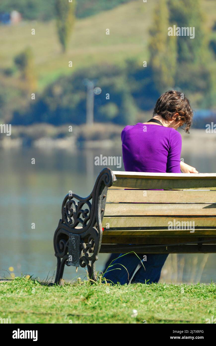 Un colpo retroguidato di una donna seduta su una panca esterna vicino ad un lago in Cile. Foto Stock