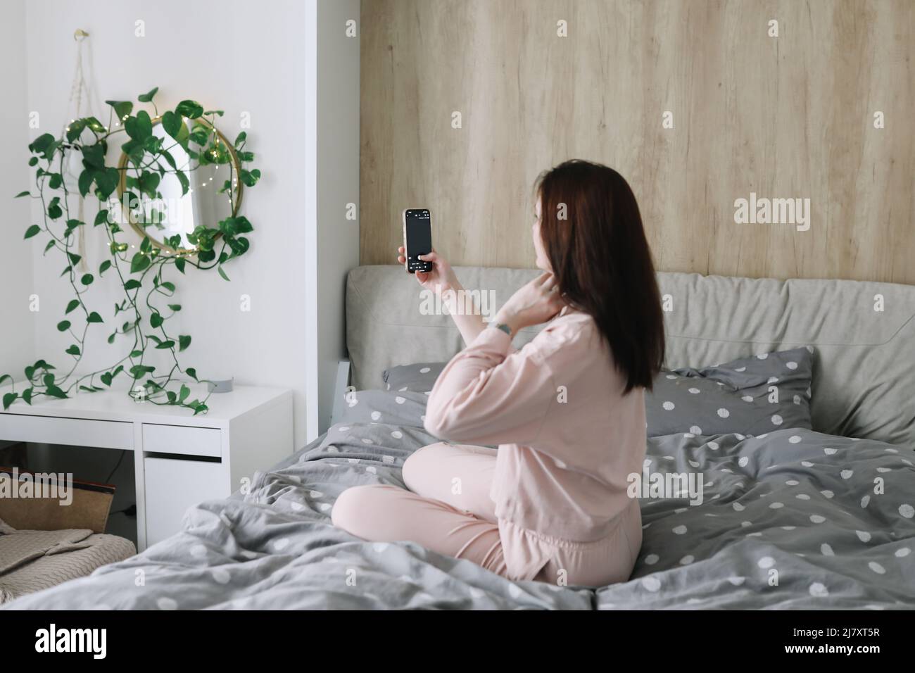 Bella donna seduta a letto e prende selfie Foto Stock