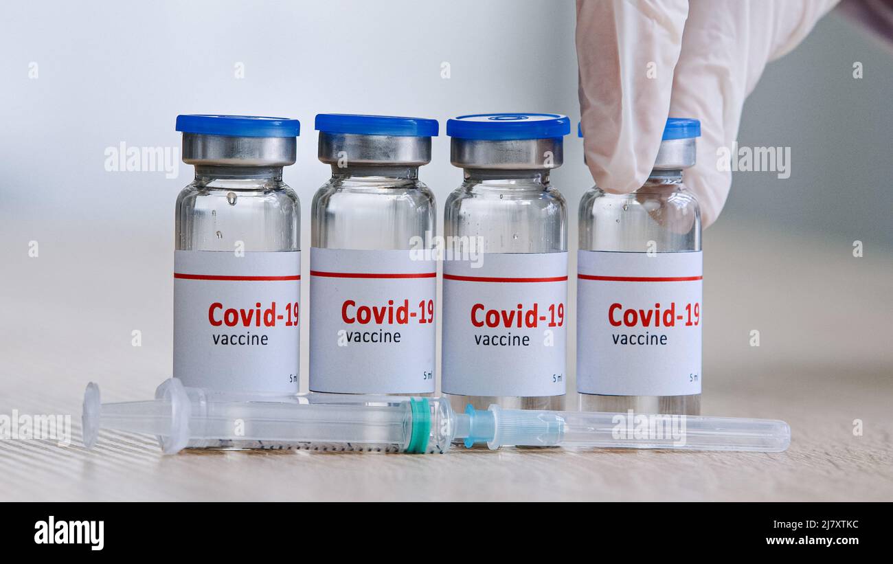 Primo piano dettaglio di quattro bottiglie di vetro con vaccino covid19 contro la pandemia di coronavirus su un tavolo di legno in un laboratorio vicino alla siringa mano in Foto Stock
