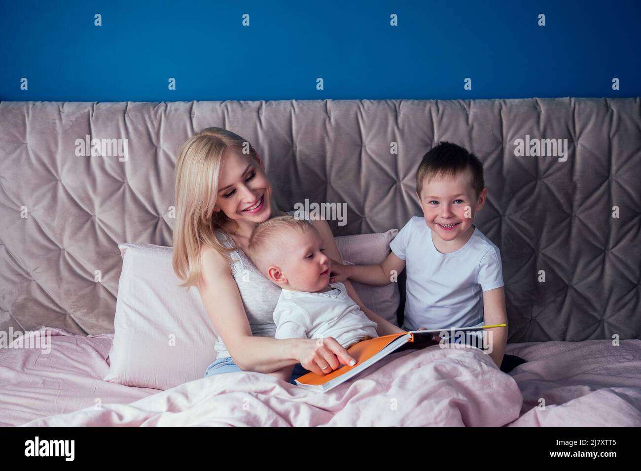 La famiglia si diverte insieme al fine settimana.madre e due bambini a letto. Mamma bionda e ragazzi che giocano in camera da letto del mattino. Genitore e poco Foto Stock