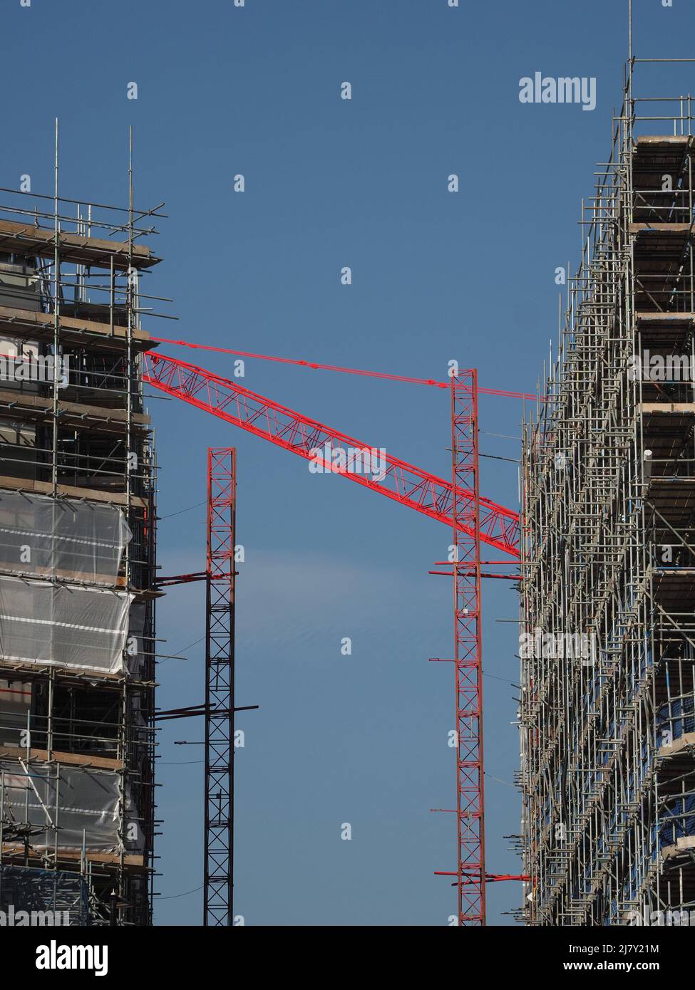La gru di colore rosso brillante colma il divario tra 2 nuovi e alti edifici in costruzione nel centro di Sheffield, Yorkshire, Inghilterra, Regno Unito Foto Stock
