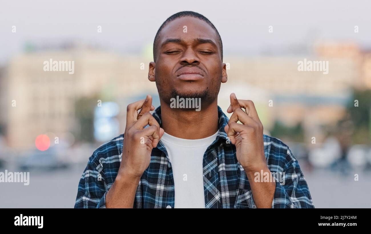 Il giovane uomo di speranza afroamericano si trova in città sulla strada che attraversa le dita pregare dice la preghiera spera per la possibilità futura, speranza concetto di fede Foto Stock