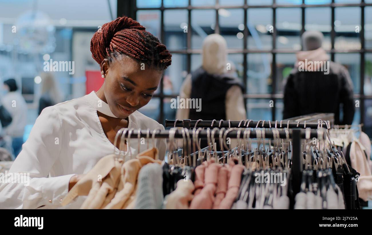 Ritratto serio messo a fuoco giovane ragazza shopper femmina consumatore corre attraverso rack african american donna scelta vestiti nel centro commerciale di acquisto Foto Stock