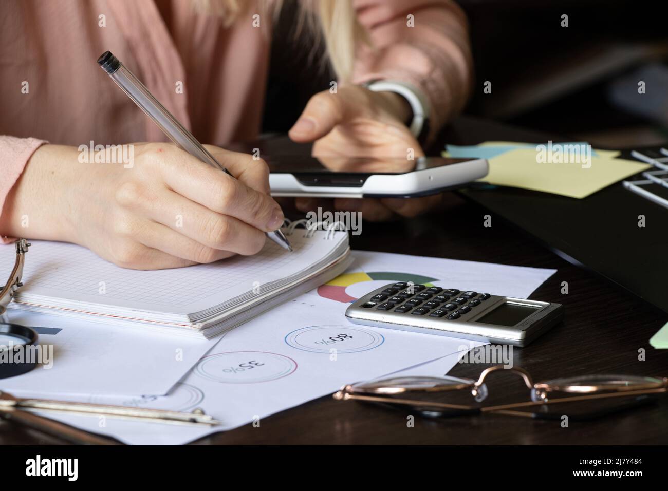 La ragazza tiene il telefono nelle sue mani e fa un grafico a barre e rapporti sul robot al tavolo, il commercio e la finanza, la tecnologia e le vendite in linea Foto Stock