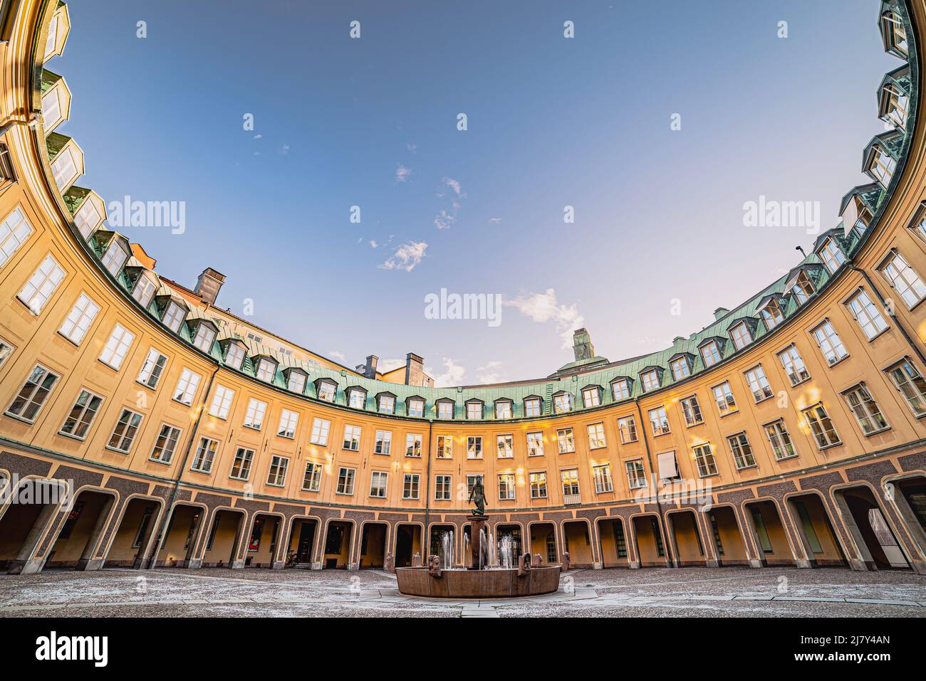 Edificio di forma rotonda e ordinato che avvolge una piccola piazza acciottolata. Architettura elegante e raffinata con struttura ad arco circolare che circonda una piccola piazza signorile Foto Stock