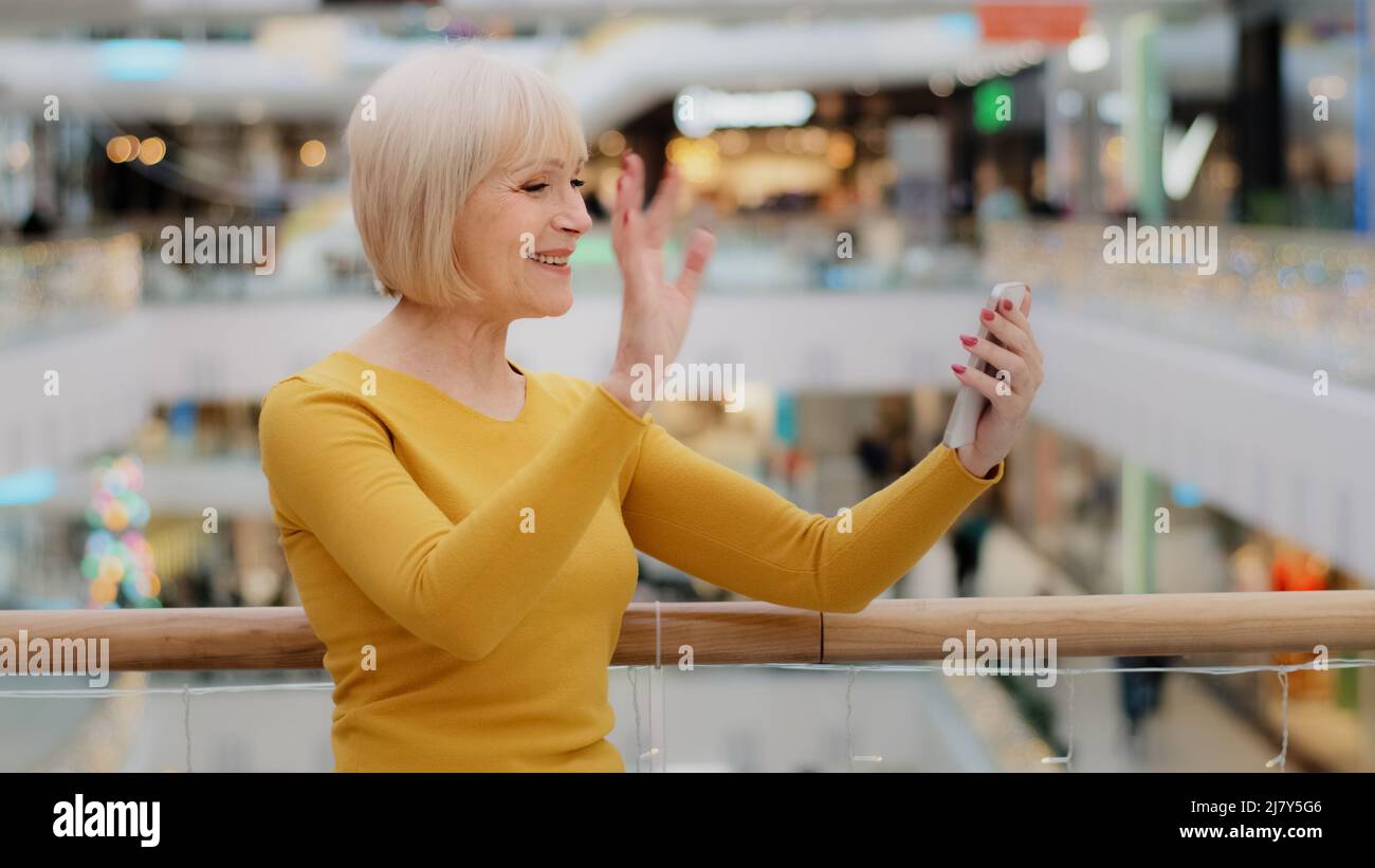 Donna matura di mezza età che tiene lo smartphone a portata di mano parlando con la videochiamata utilizzando l'app mobile per la conferenza sorridendo e salutando i gesti Foto Stock