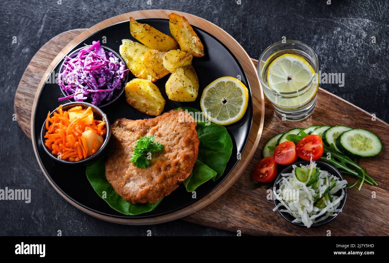 Cotoletta di maiale impanata ricoperta di pangrattato con patate e insalate di verdure Foto Stock