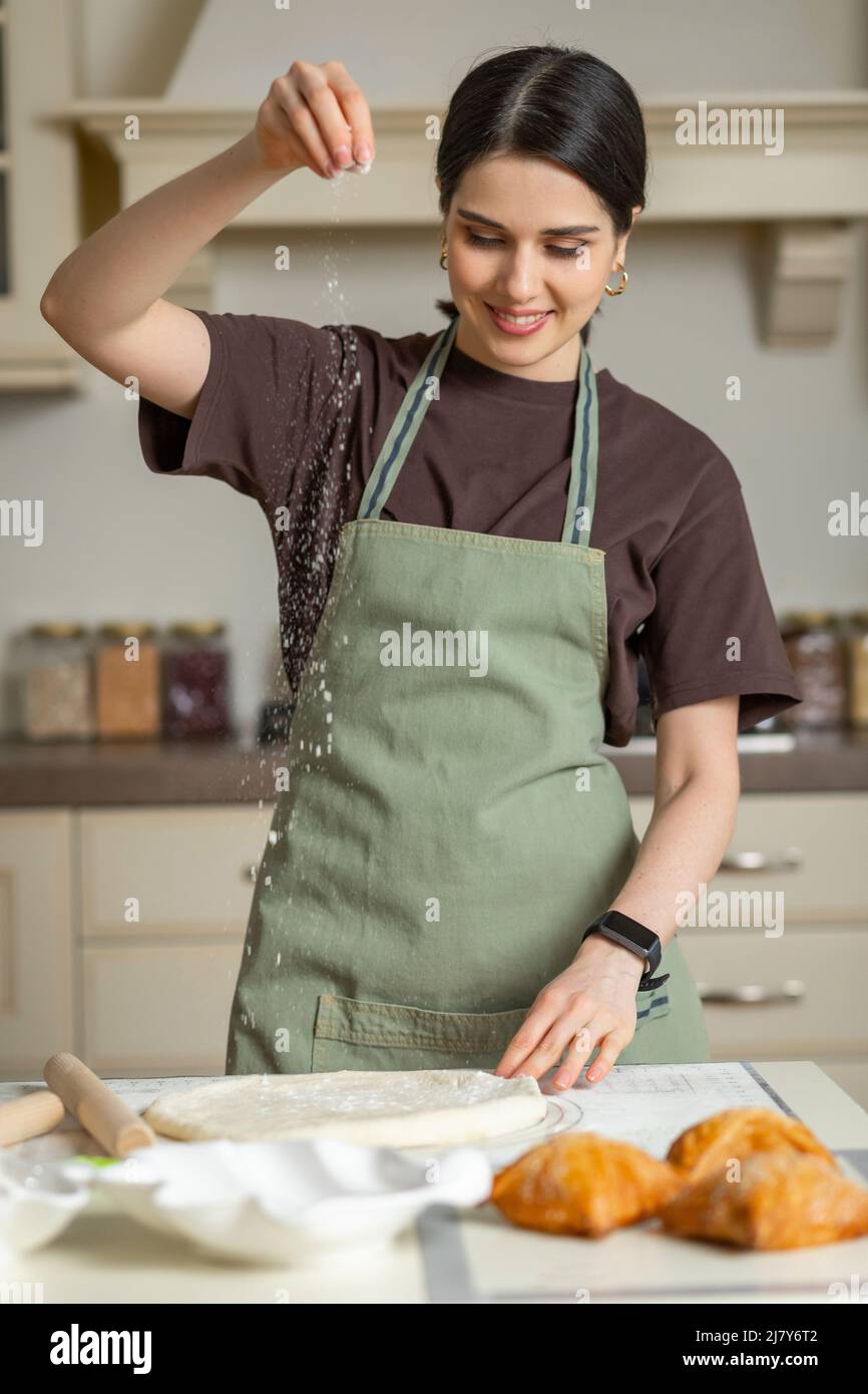 Bella giovane bruna sorridente donna gara mista in una cucina grembiule sta cucinando la cottura fatta in casa in cucina Foto Stock