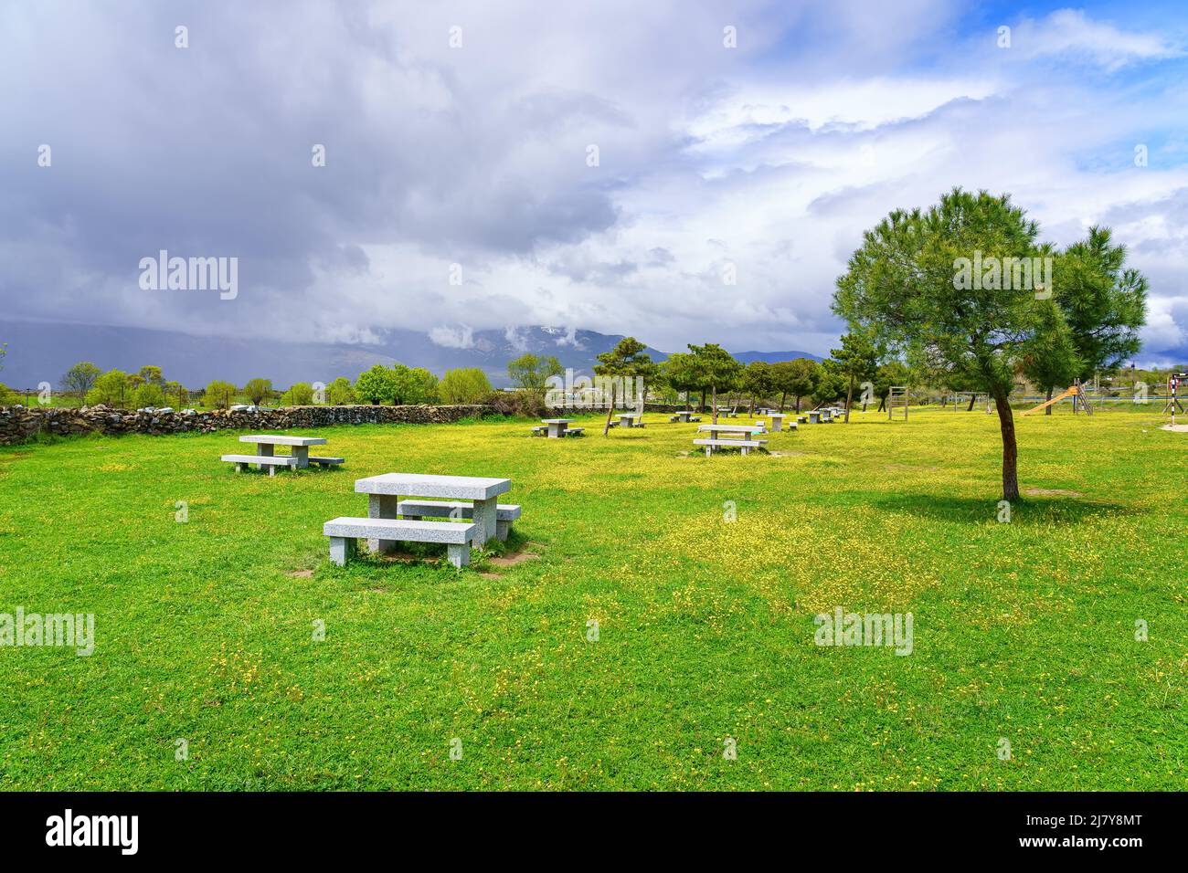 Panchine di pietra per sedersi nel parco di erba verde e fiori gialli, Guadarrama Madrid. Foto Stock