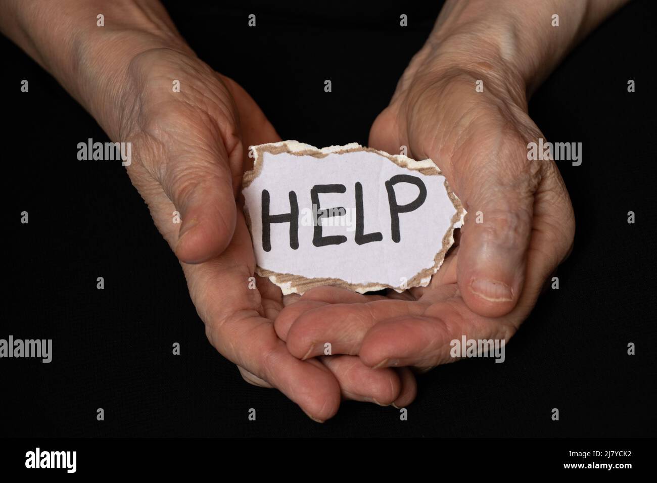 Le vecchie mani femminili tengono un pezzo di carta con testo di aiuto nel buio, aiutano le persone nel bisogno, una persona nel bisogno Foto Stock