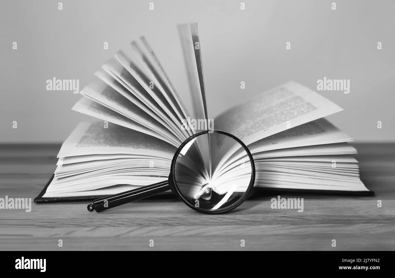 Apri libro con lente d'ingrandimento. Rotazione delle pagine. Ricerca e analisi delle informazioni, concetto di conduzione della ricerca. Bianco e nero. Foto di alta qualità Foto Stock